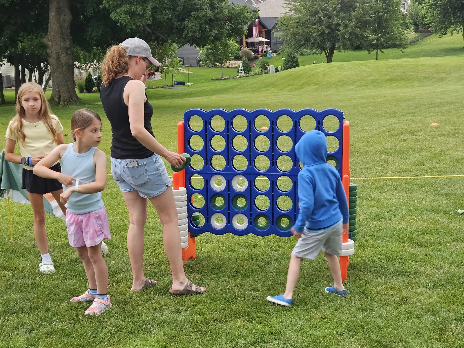 Kids and a parent playing a giant Connect Four game on the golf course lawn