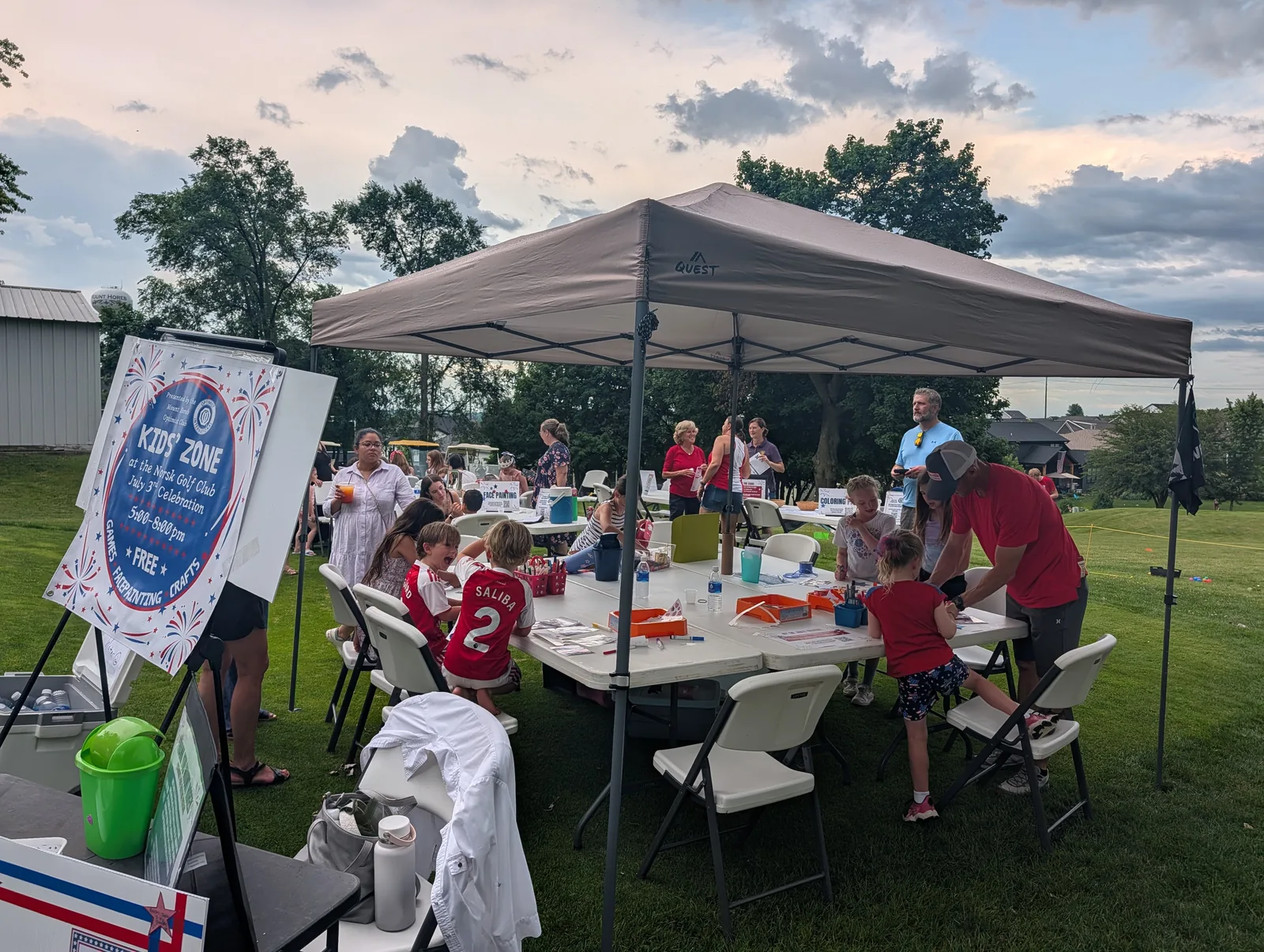 The Kid's Zone craft tent at dusk with families gathered under it