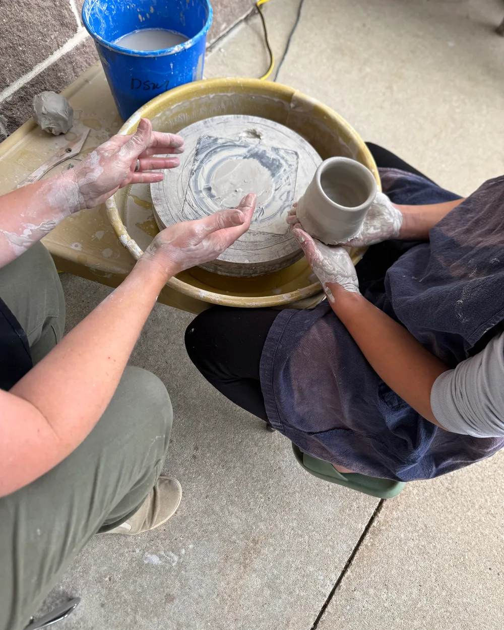 A freshly thrown clay mug held at the pottery wheel, a potter's hands alongside