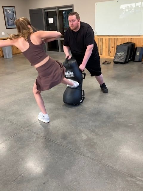 A participant landing a kick on a padded trainer at the self-defense class